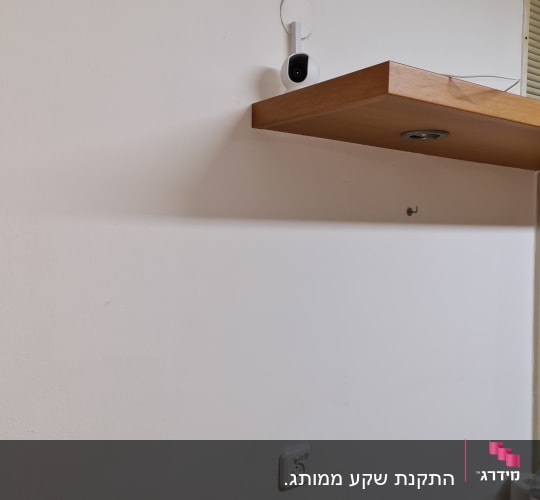שקע חשמל על קיר לבן מתחת למדף עץ